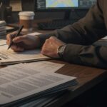 書類にペンを走らせるー男性の腕ーとー机上の文書ーが映った写真