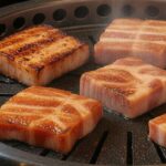 厚切り豚バラを網で焼く焼肉の様子。表面にこんがり焼き目がついたジューシーな肉が並ぶ。